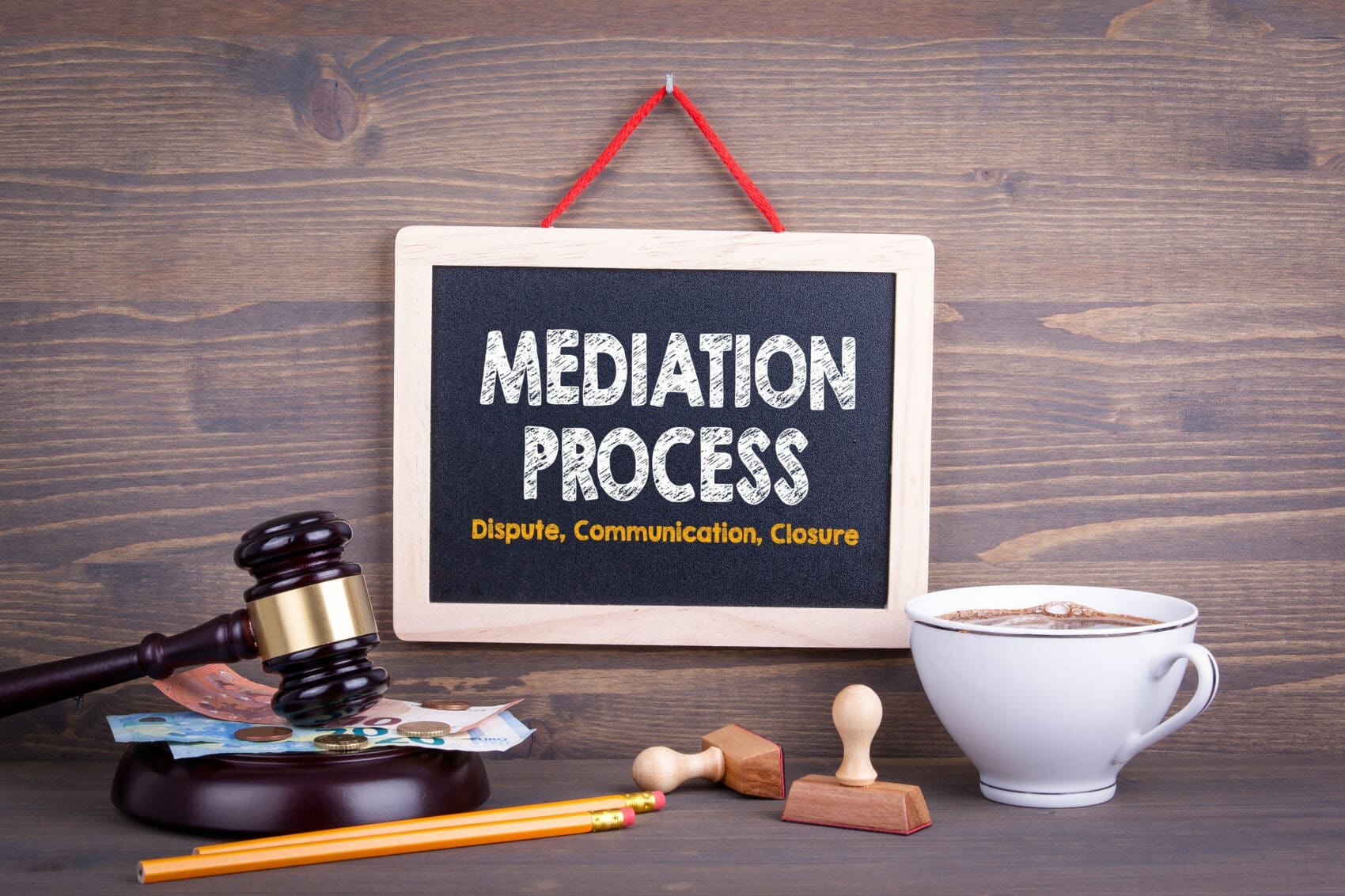 Signboard Reads 'mediation Process' with Subtitle 'dispute, Communication, Closure' on a Wooden Background; Includes Gavel, Money, Coffee Cup and Desk Items Nearby.