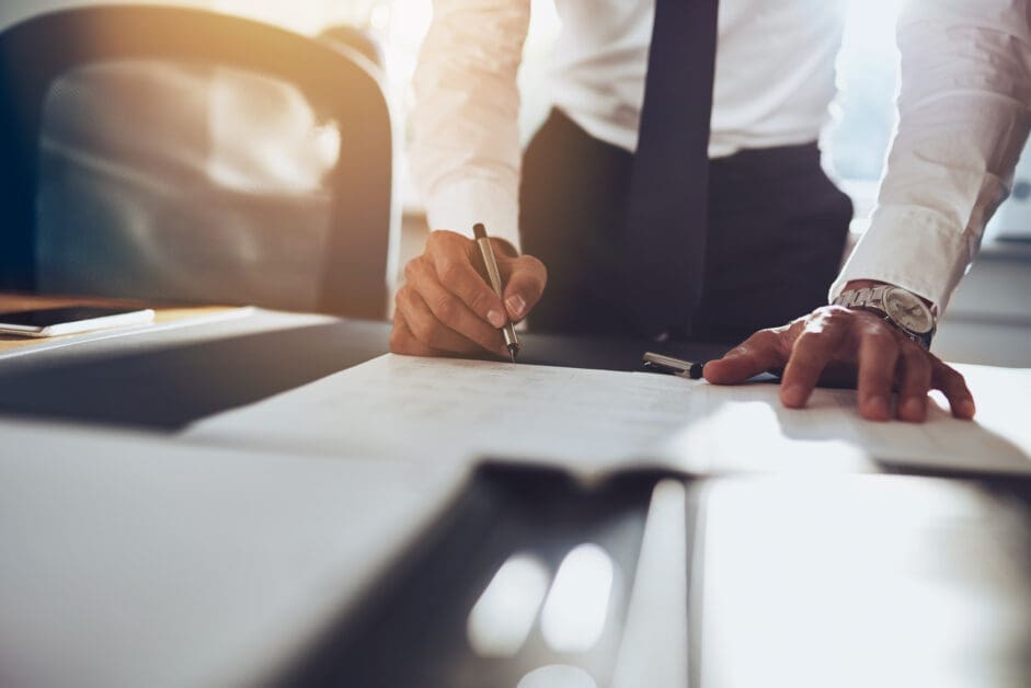 Businessperson Signing a Document at a Desk, with Sunlight in the Background.